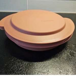 Könnte beinhalten: Ein pfirsichfarbener Tupperware-Behälter mit Deckel. Der Behälter hat eine runde Form mit zwei Griffen an den Seiten. Der Deckel ist leicht gewölbt und passt gut oben drauf. Der Behälter besteht aus Kunststoff.