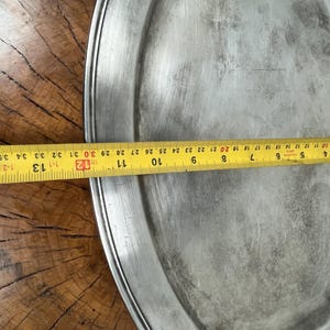May include: A large, round, silver serving platter with a raised rim. The platter is slightly dented and has a worn, aged appearance.