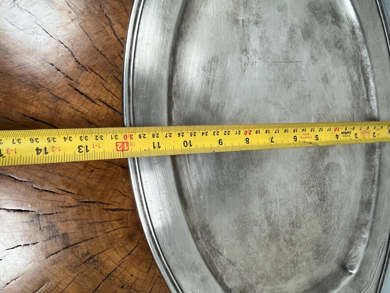 May include: A large, round, silver serving platter with a raised rim. The platter is slightly dented and has a worn, aged appearance.