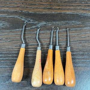 Peut inclure: Ensemble de six crochets avec manches en bois et crochets en métal. Les manches sont de couleur marron clair et les crochets sont argentés. Les crochets sont disposés en rangée, pointes vers le haut. Pour travaux manuels.