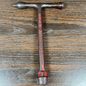 Könnte beinhalten: Ein Vintage-Werkzeug in T-Form mit roter und schwarzer Oberfläche. Das Werkzeug hat ein spitzes Ende und einen Griff mit dem Text "REAL HUDY". Das Werkzeug wird wahrscheinlich für Automobil- oder mechanische Arbeiten verwendet.