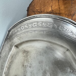 May include: A silver serving platter with a decorative floral design around the edge.