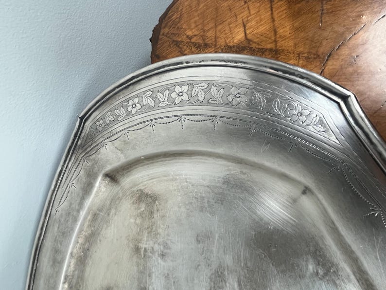 May include: A silver serving platter with a decorative floral design around the edge.