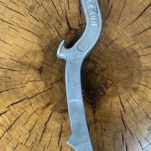 May include: A silver bottle opener with the word "AKRON" embossed on the handle. The opener has a curved design with a loop at the top and a pointed end. The number "451/2" is also visible.