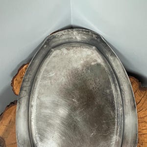 May include: A silver oval serving tray with a slightly raised rim. The tray has a brushed finish and shows signs of wear.