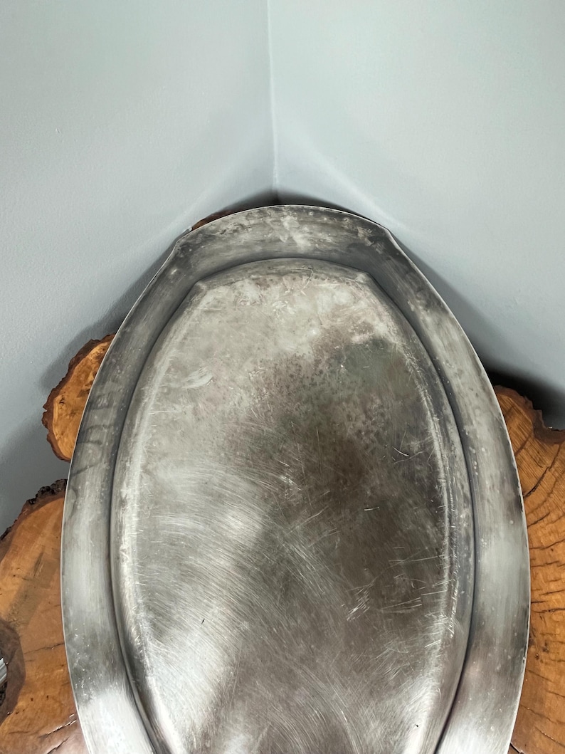 May include: A silver oval serving tray with a slightly raised rim. The tray has a brushed finish and shows signs of wear.