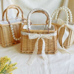 May include: Three woven wicker baskets with handles. The basket on the left has a pearl necklace handle. The middle basket has a white lace bow and a white lace handle. The basket on the right has a white satin ribbon and a pearl necklace handle.