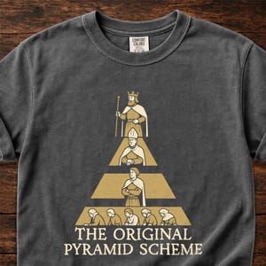 May include: A charcoal gray crew neck t-shirt featuring a graphic print of a social hierarchy arranged in a pyramid shape. The design includes a king, a religious figure, a noble, and commoners, with the text "THE ORIGINAL PYRAMID SCHEME" below.