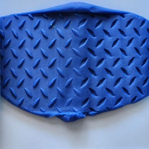 May include: A blue clay sheet with a diamond pattern is positioned between two light blue rollers, also with the diamond pattern. The clay sheet is a darker shade of blue and has a textured surface. The rollers are a lighter shade of blue.