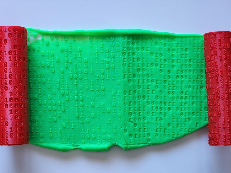 May include: A bright green sheet embossed with binary code, with two red cylindrical rollers on either side, also showing binary digits. The tools suggest a theme of technology or data processing, possibly for crafting or artistic projects.