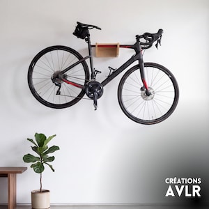 May include: A black road bicycle with red accents is mounted on a light-coloured wooden wall rack. The bicycle features drop handlebars, a black saddle bag, and a water bottle cage. The text CRÉATIONS AVLR is visible in the bottom right corner.