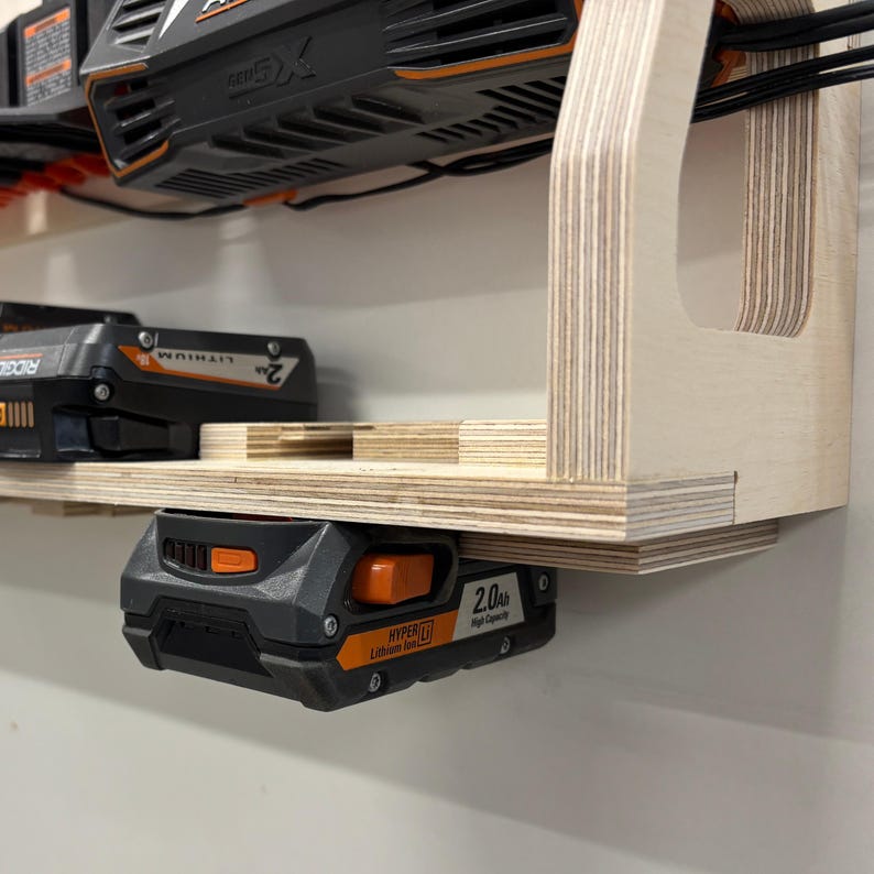 May include: A wooden power tool organizer with multiple shelves and slots. The organizer holds black and orange power tool batteries and tools. The batteries are labeled "2.0 Ah" and "Hyper Lithium".