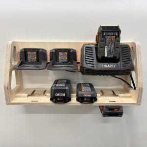May include: A wooden power tool organizer with multiple charging stations and battery storage. The organizer holds several black and orange RIDGID chargers and batteries. The wooden shelf is mounted on a white wall.