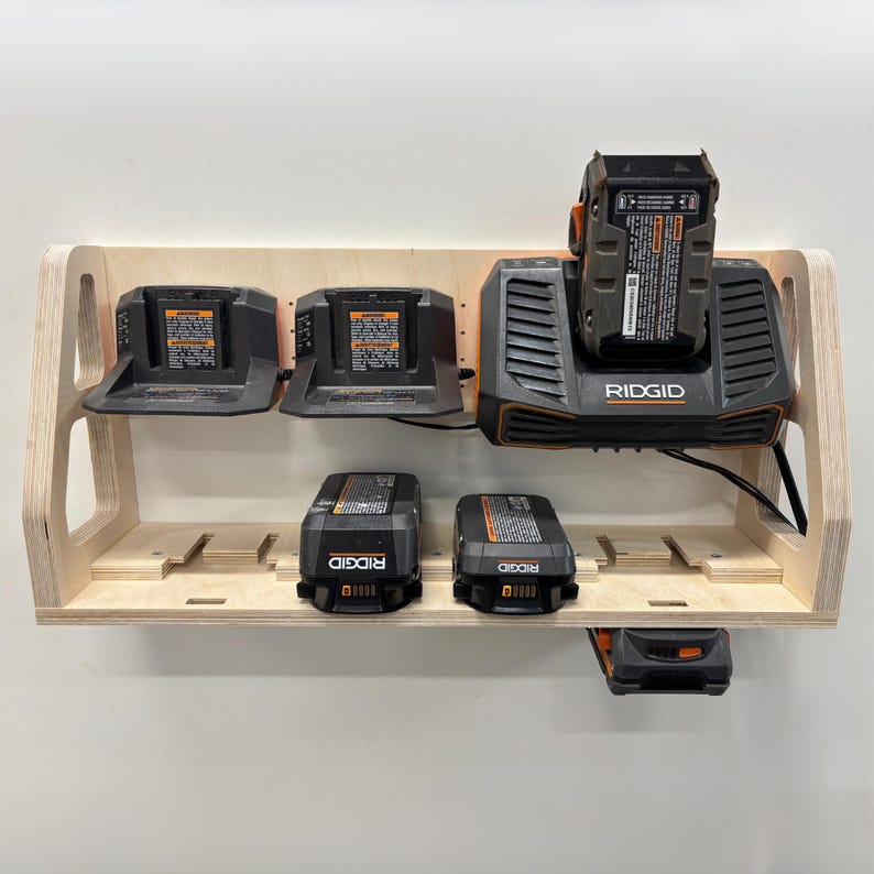 May include: A wooden power tool organizer with multiple charging stations and battery storage. The organizer holds several black and orange RIDGID chargers and batteries. The wooden shelf is mounted on a white wall.