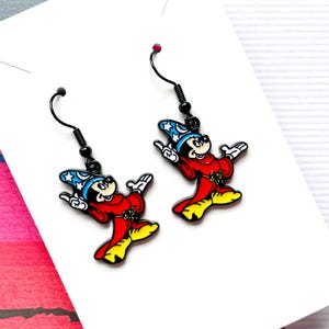 May include: A pair of black dangle earrings featuring a cartoon image of Mickey Mouse dressed as a sorcerer. Mickey is wearing a red robe, a blue hat with stars, and a mischievous grin.