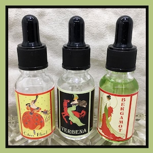 May include: Three glass bottles with dropper tops and labels. The labels feature illustrations of women in vintage clothing and the text "Citrus Blend", "Verbena", and "Bergamot".