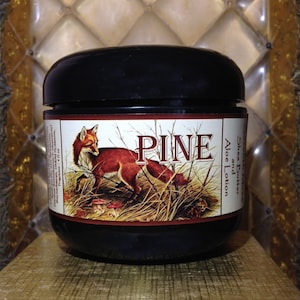 May include: A black jar with a brown label featuring a red fox in a woodland setting. The label reads "PINE Shea Butter Aloe and Lotion".