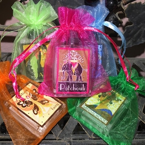 May include: Four small glass bottles with different scents in organza bags. The scents are Autumn Fairy, Patchouli, Sandalwood, and another scent with a picture of a woman on the bottle.
