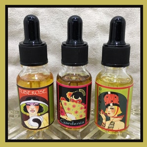 May include: Three glass bottles with black dropper tops and labels featuring vintage illustrations of women and floral names. The labels are green, red, and pink with black text. The bottles contain a clear liquid. The labels read "Tuberose", "Gardenia", and "Plumeria".