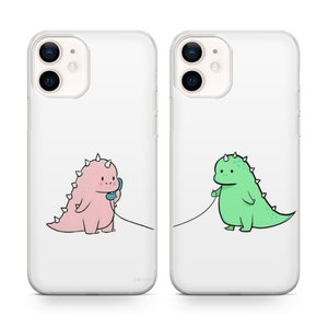 May include: Two clear phone cases with a cartoon dinosaur design. One case features a pink dinosaur on the phone, the other a green dinosaur. Both dinosaurs are connected by a phone cord.