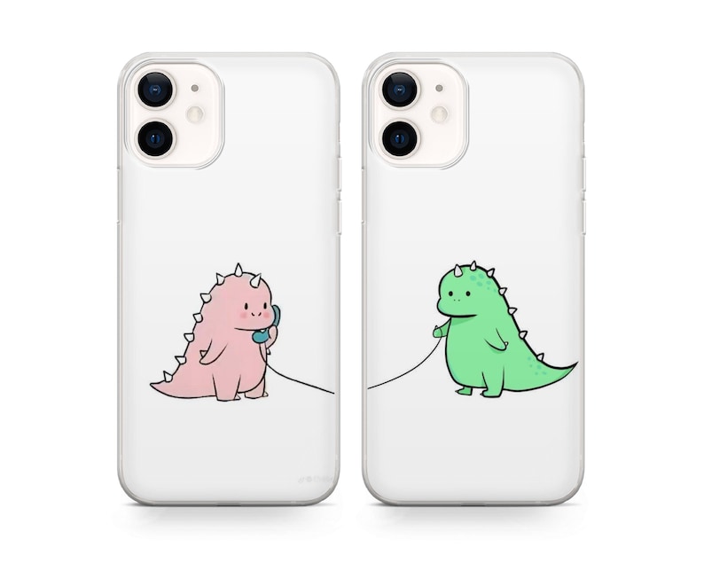 May include: Two clear phone cases with a cartoon dinosaur design. One case features a pink dinosaur on the phone, the other a green dinosaur. Both dinosaurs are connected by a phone cord.