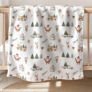 May include: White baby blanket with a repeating pattern of Christmas-themed illustrations. The illustrations include Santa Claus, elves, reindeer, Christmas trees, candy canes, and a truck with a Christmas tree on top. The name "Oliver" is repeated throughout the pattern.
