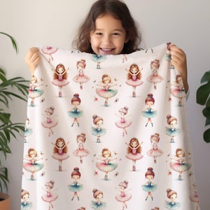 May include: A white fleece blanket with a repeating pattern of watercolor ballerina girls in pink, blue, and green dresses. The ballerinas are all wearing pink shoes and have brown hair. There are also small butterflies and flowers scattered throughout the pattern.