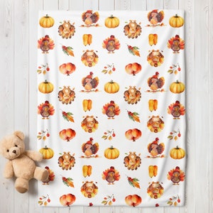May include: White blanket with a repeating pattern of cartoon turkeys, pumpkins, and fall foliage. The turkeys are wearing hats and are in various poses. The pumpkins are orange, and the leaves are red and yellow. A teddy bear is in the lower left corner.