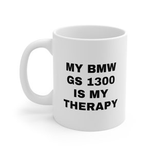 以下が含まれることがあります： 白いセラミック製のコーヒーカップで、黒い文字で「MY BMW GS 1300 IS MY THERAPY」と書かれています。