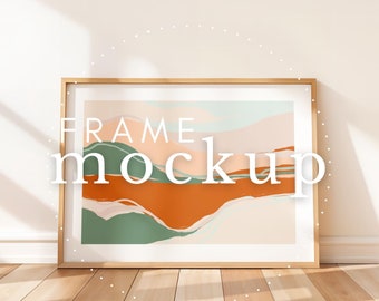 May include: A wooden frame mockup with a colorful abstract painting inside. The painting features shades of orange, green, and blue, creating a modern and artistic look. The frame is placed on a wooden floor with natural light shining through a window.