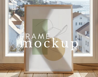 May include: A framed art print with a minimalist line drawing of a person wearing a hat, set against a green rectangle and a yellow circle. The words "FRAME mockup" are printed in white. The frame is made of light-colored wood.