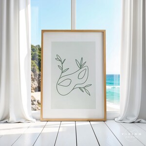 May include: A framed print with a minimalist line drawing of a masquerade mask with leaves on a light green background.