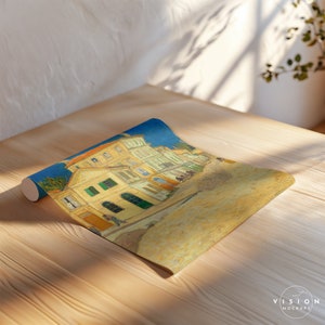 May include: A rolled up poster print of a painting depicting a yellow building with green shutters and a blue sky. The building is in a town square with other buildings in the background. The painting is in a style reminiscent of Vincent van Gogh.