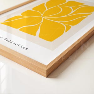 May include: A framed print with a yellow abstract design of a flower with curved lines. The print is on a cream background and has the text "Art Collection" in the bottom left corner.