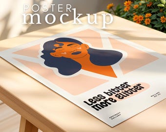 May include: A white poster mockup with a pink and orange illustration of a woman with long dark hair. The text on the poster reads "Less bitter more glitter".