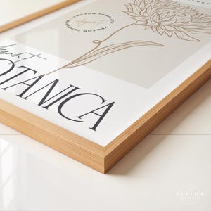 May include: A framed print with a beige background and a line drawing of a flower in brown. The text "Botanica" is printed in black at the bottom of the print.