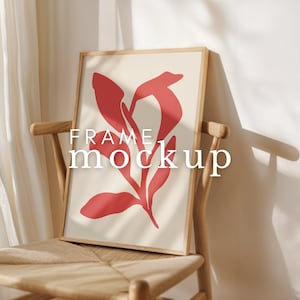 May include: A wooden frame mockup with a red abstract floral design on a cream background. The frame is leaning against a wooden chair with a woven seat.