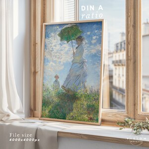 May include: A framed painting of a woman in a white dress holding a green umbrella, standing in a field of flowers with a child in the background. The painting is in a wooden frame and is hanging on a wall.
