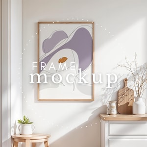 Puede incluir: Una impresión artística enmarcada con un dibujo lineal minimalista de la cara de una mujer con sombrero, con acentos lavanda y naranja. La obra de arte está en un marco de madera clara. El texto "FRAME mockup" está superpuesto.