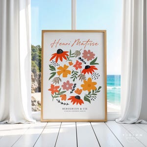 May include: A framed print with a white background and a colorful illustration of flowers in shades of orange, yellow, pink, and green. The text "Henri Matisse" is at the top of the print, and the text "Berggruen & Cie" is at the bottom.