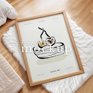 May include: A framed illustration of a stylized apple with a bowl underneath. The frame is made of natural wood and has a white mat. The illustration is on a cream background with the text "FRAME MOCKUP" and "BLACK INK" in black.