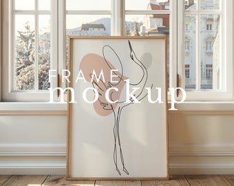 May include: A framed print of a minimalist line drawing of a crane with a pink and beige abstract background. The frame is light brown wood and the print is on white paper. The text "FRAME MOCKUP" is superimposed on the image.