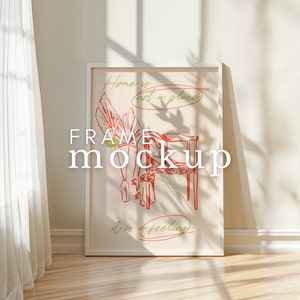 May include: White frame mockup with a beige background and a red and green illustration of a chair and a person with the text "Home is not a place it is a feeling".