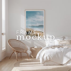 May include: A white bed with a white duvet cover and a beige throw pillow. A wicker chair sits in the corner of the room, and a framed photo of a beach scene hangs on the wall. The text "FRAME mockup" is superimposed on the image.