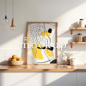 Może przedstawiać: Oprawiony wydruk artystyczny z minimalistycznym rysunkiem kobiety, zaakcentowany żółtymi i czarnymi kształtami. Drewniana rama stoi na drewnianym blacie w kuchni. Na obrazie nałożony jest tekst "FRAME mockup".