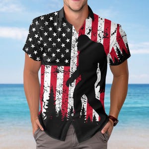 May include: Short-sleeved button-down shirt featuring a distressed American flag design with a black silhouette of Bigfoot. The shirt has a black collar and buttons, and is made of a lightweight fabric.