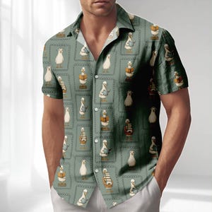 Puede incluir: Camisa de manga corta con botones con un patrón repetido de gansos de dibujos animados leyendo libros. La camisa tiene un fondo verde claro con los gansos en cuadrados enmarcados individuales. Los gansos llevan sombreros y gafas.