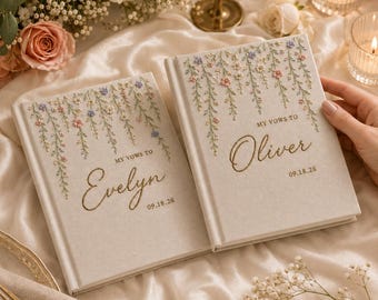 May include: Two off-white hardcover vow books featuring embroidered floral vines in pink, blue, and green. The left book reads "MY VOWS TO Evelyn 09.18.26" and the right book reads "MY VOWS TO Oliver 09.18.26" in gold script lettering.