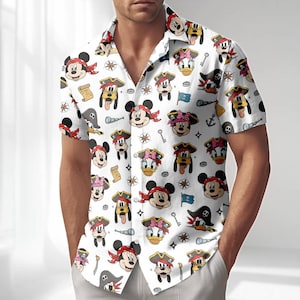 Könnte beinhalten: Weißes kurzärmeliges Hemd mit einem sich wiederholenden Muster von Cartoon-Piratenfiguren, darunter Micky Maus, Minnie Maus, Donald Duck und Goofy. Die Figuren tragen Piratenhüte und Bandanas, mit nautischen Elementen wie Ankern und Schatzkarten.