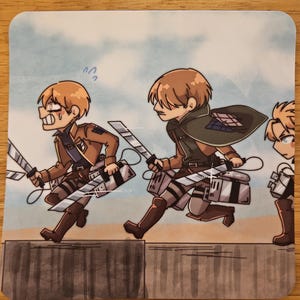 Puede incluir: Posavasos cuadrado con una ilustraci&oacute;n de estilo anime de tres personajes con uniformes marrones y espadas, corriendo. El fondo es un cielo azul claro con un muro gris en primer plano. Los personajes tienen cabello casta&ntilde;o.
